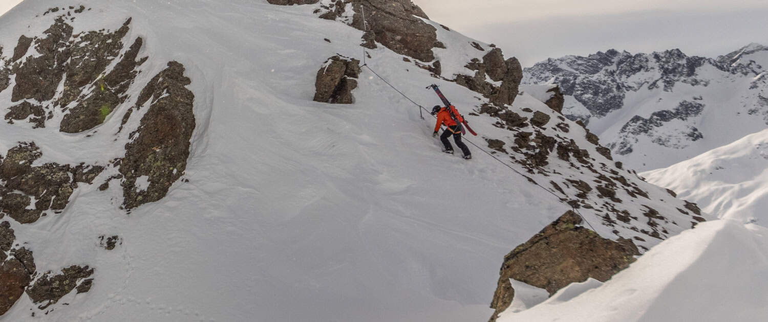 Adventurer navigating the secured steel cable section of the winter via ferrata in St. Anton, surrounded by deep snow and dramatic Arlberg mountain scenery. Via Ferrata St. Anton Winter Route with Steel Safety Cable